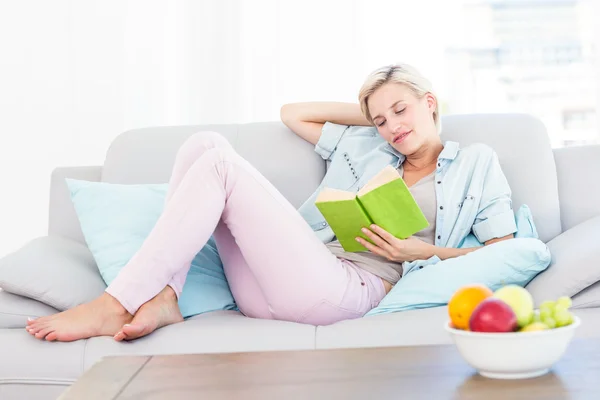 Donna bionda che legge un libro sul divano — Foto Stock