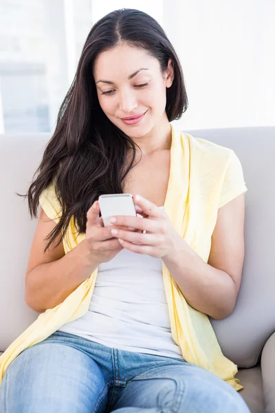 Půvabná brunetka pomocí smartphone na gauči — Stock fotografie