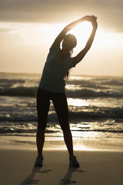 Brune sportive s'étirant sur la plage — Photo