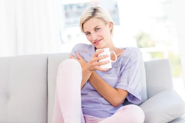 Donna bionda sul divano con in mano una tazza — Foto Stock