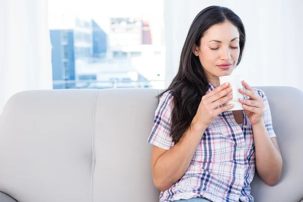 Brünette hält Heißgetränk auf Couch — Stockfoto