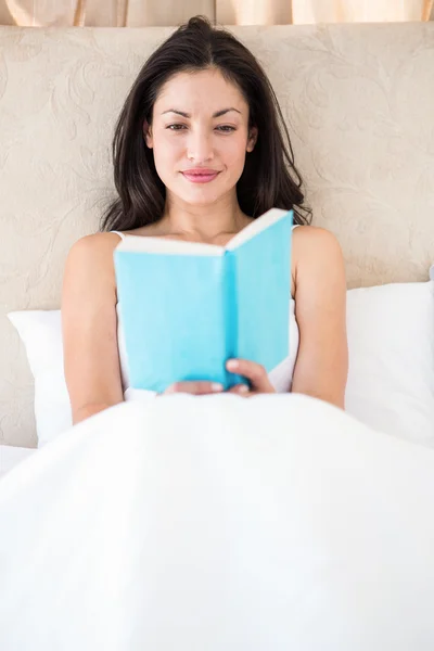 Hezká brunetka čtení na posteli — Stock fotografie