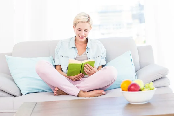 Mulher loira lendo um livro no sofá — Fotografia de Stock