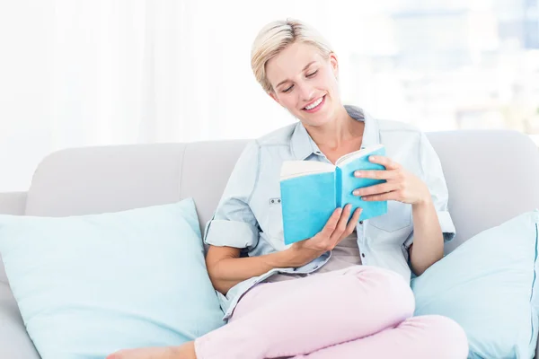 Blonďatá žena čte knihu na gauči — Stock fotografie