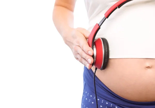 Беременная женщина держит наушники над шишкой — стоковое фото