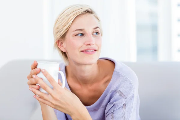 Blond kvinna på soffan håller en mugg — Stockfoto