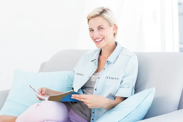Blond kobieta czyta czasopisma na kanapie — Zdjęcie stockowe