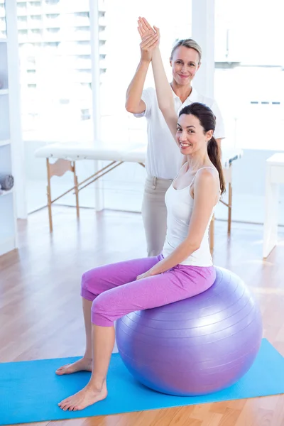 Trainer helping woman on exercise ball — Stock Photo, Image