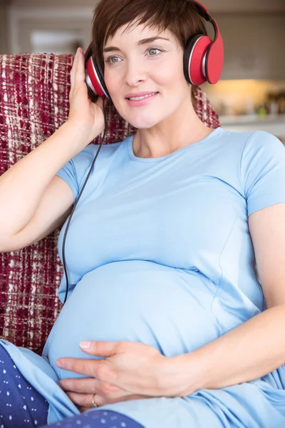 Hamile kadın üzerinde şişlik kulaklıklar koyarak — Stok fotoğraf