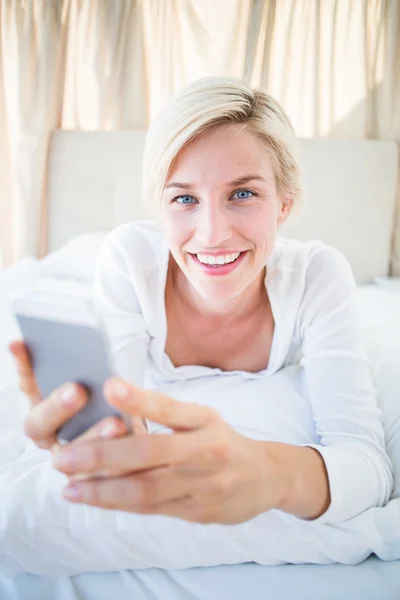 Blondine liegt im Bett und schreibt SMS mit dem Handy — Stockfoto
