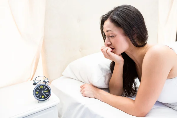 Morena viendo reloj despertador en la cama — Foto de Stock