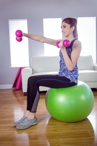 Подходящая женщина поднимает гантели на мяче для упражнений — стоковое фото