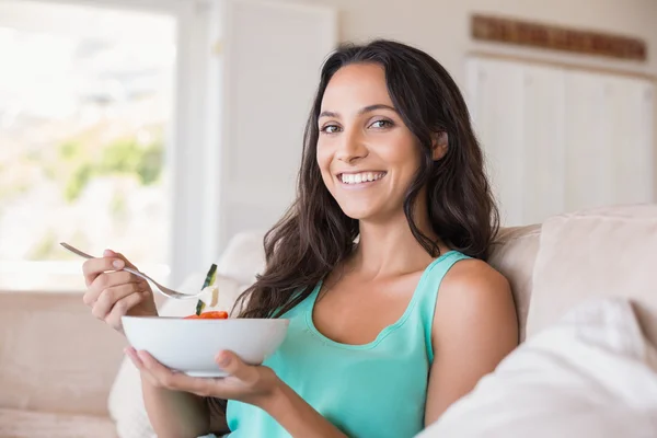 Bella bruna mangiare insalata sul divano — Foto Stock