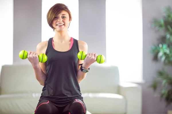 Fit woman lifting dumbbell sitting on ball — Stock Photo, Image