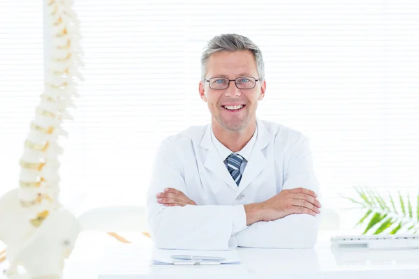 Docteur assis à son bureau souriant à la caméra — Photo