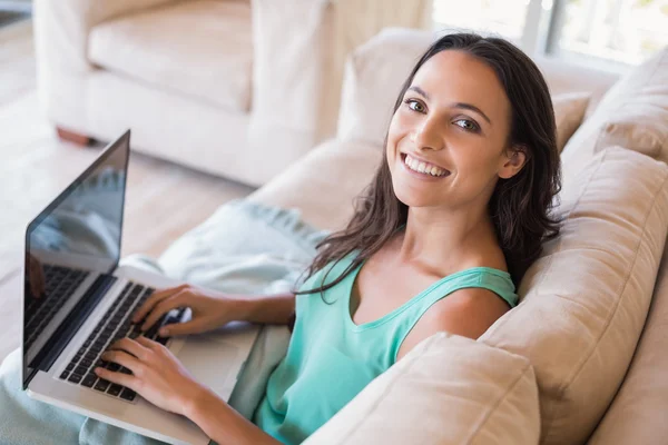 Bruneta pomocí její laptop na gauči — Stock fotografie