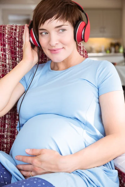 Mujer embarazada poniendo auriculares sobre golpe — Foto de Stock