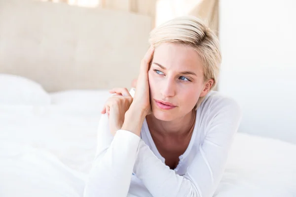 Thoughtful blonde woman lying on bed — Stock Photo, Image