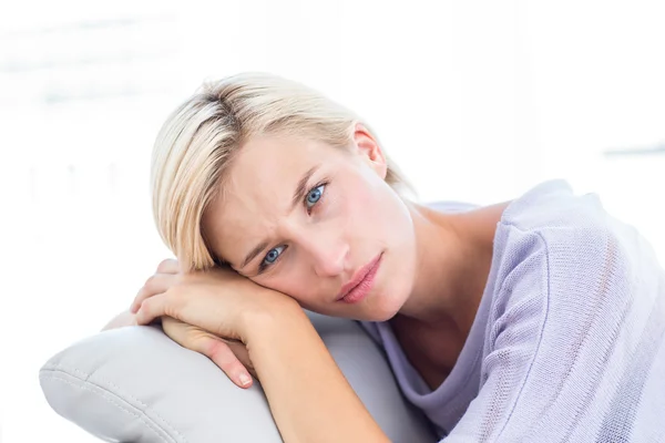 Thoughtful blonde woman sitting on the couch — Stock Photo, Image