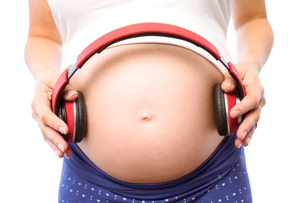 Беременная женщина держит наушники над шишкой — стоковое фото