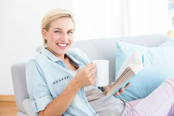 Söt blond kvinna läser en bok och hålla en mugg — Stockfoto