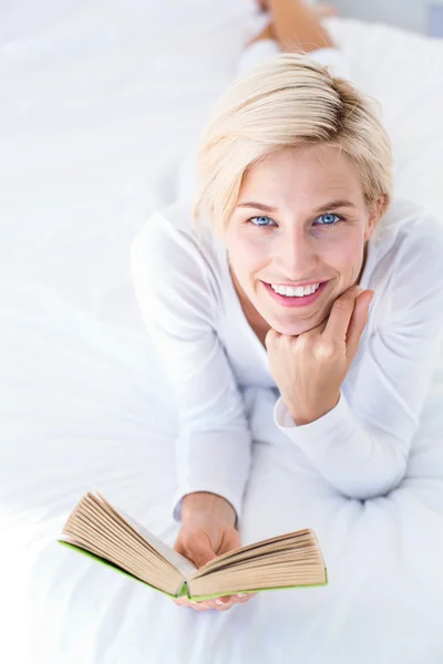 Mujer rubia acostada en la cama y leyendo — Foto de Stock