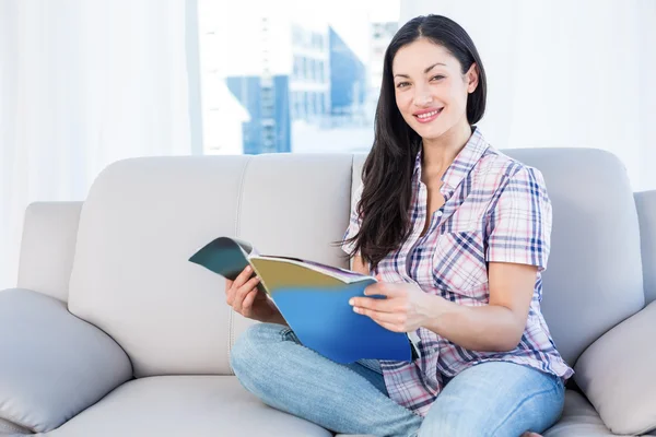 Morena segurando uma revista no sofá — Fotografia de Stock