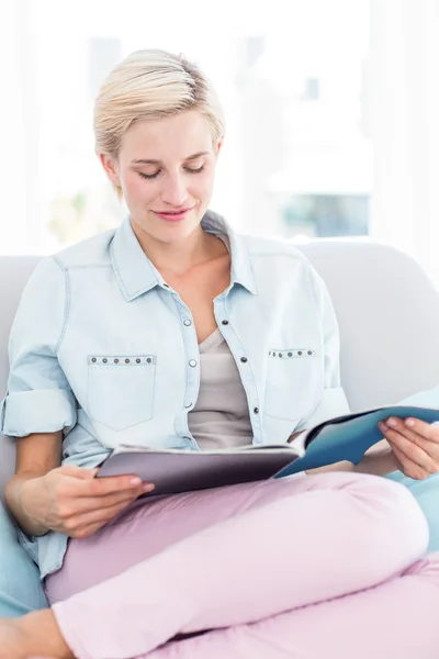 Mulher loira lendo uma revista no sofá — Fotografia de Stock