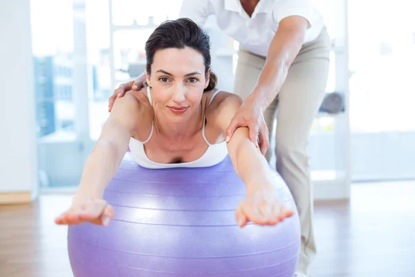 Trainer helping woman on exercise ball — Stock Photo, Image