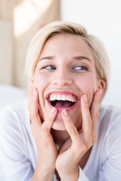 Lachende blonde vrouw liggend op het bed — Stockfoto