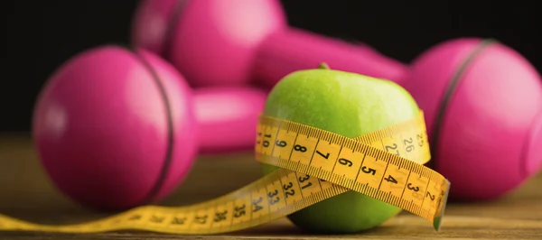Pink dumbbells with green apple and measuring tape — Stock Photo, Image