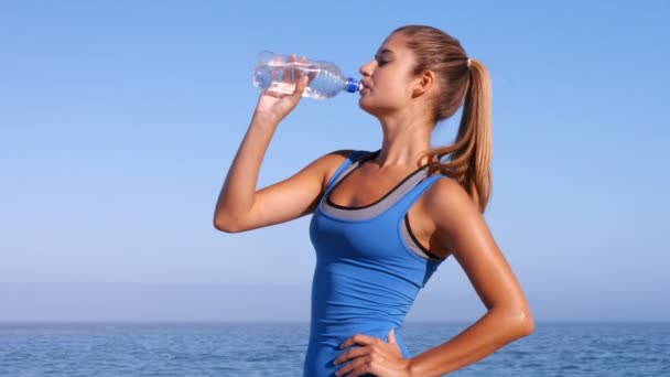 Подходящая женщина пьет воду на пляже — стоковое видео