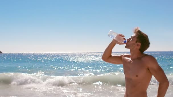 Привлекательный мужчина пьет воду на пляже — стоковое видео