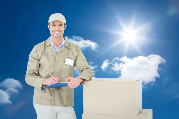 Composite image of happy delivery man writing on clipboard by ca — Stock Photo, Image