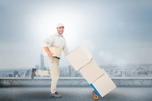 Imagen compuesta de hombre entrega feliz con carro de cajas runn —  Fotos de Stock