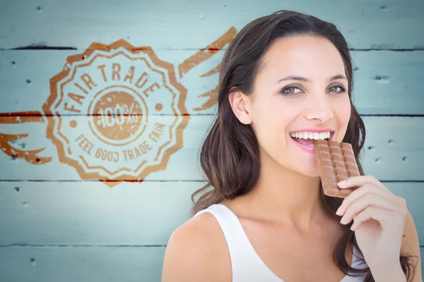 Composite image of pretty brunette eating bar of chocolate — Stockfoto