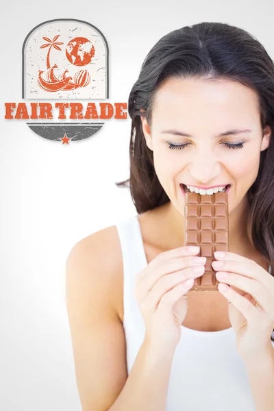 Composite image of pretty brunette eating bar of chocolate — 图库照片