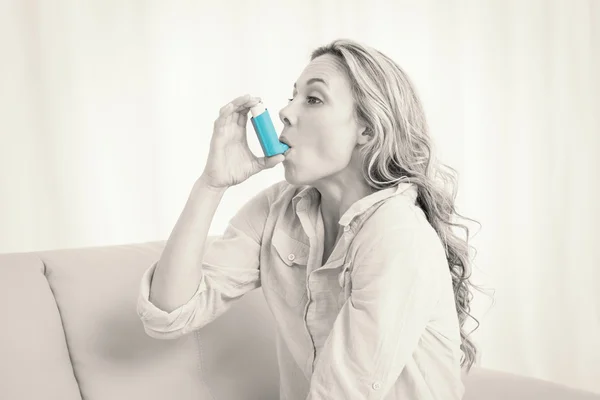 Blonde using her asthma inhaler on couch — Stock Photo, Image
