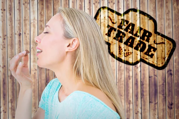 Composite image of pretty blonde eating a chocolate — Stock Photo, Image