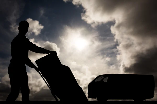 Happy delivery man pushing trolley of cardboard — Stockfoto