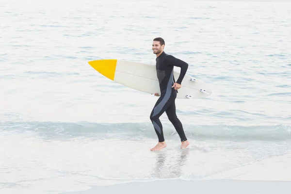 Человек в гидрокостюме с доской для серфинга на пляже — стоковое фото