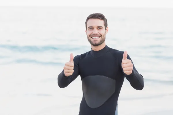 Hombre en traje de neopreno mostrando el pulgar en la playa —  Fotos de Stock