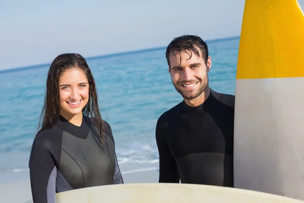 Par i våtdräkter med surfbräda på stranden — Stockfoto