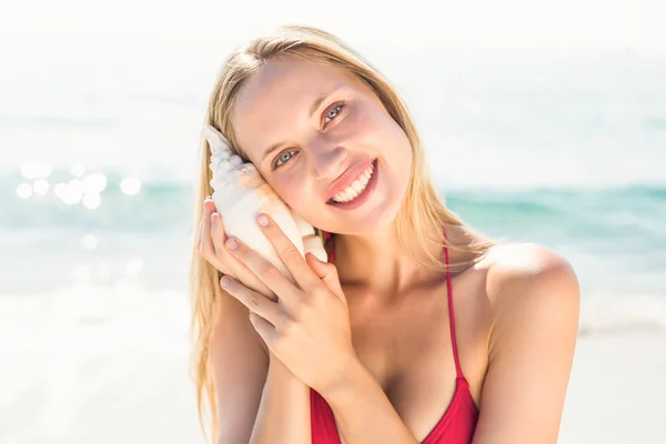 Donna bionda che ascolta conchiglia in spiaggia — Foto Stock