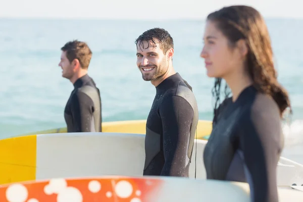 Amigos em fatos de mergulho com prancha de surf na praia — Fotografia de Stock