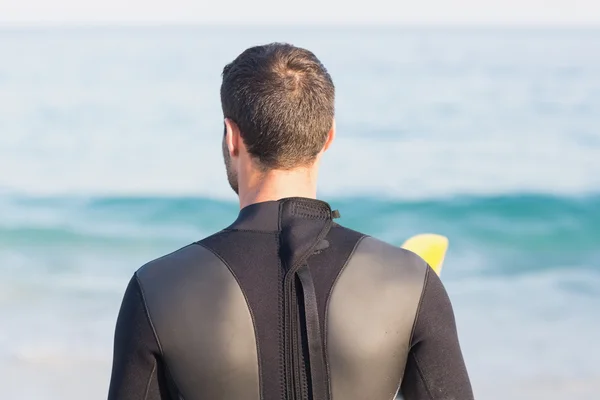 Homem de fato de mergulho com prancha de surf na praia — Fotografia de Stock