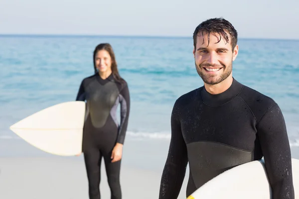 Paar in Neoprenanzügen mit Surfbrett am Strand — Stockfoto