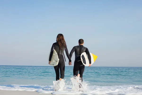 Par i våtdräkter med surfbräda på stranden — Stockfoto
