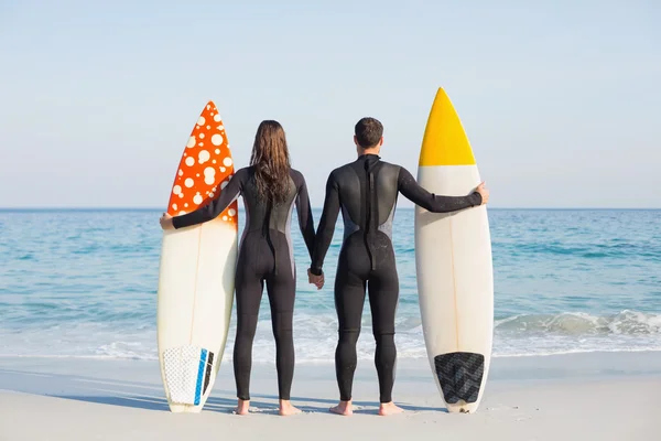 Paar in Neoprenanzügen mit Surfbrett am Strand — Stockfoto