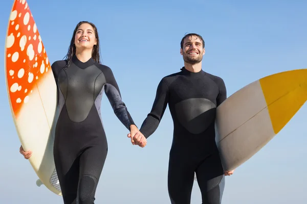Pareja en trajes de neopreno con tabla de surf en la playa — Foto de Stock